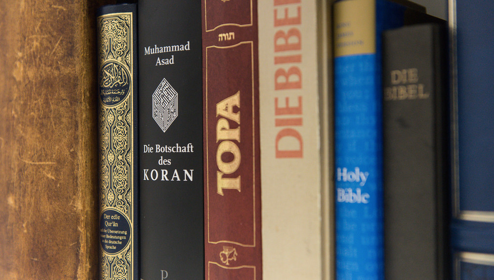 Blick auf Buchrücken verschiedener Ausgaben des Koran, der Thora und der Bibel, die nebeneinander in einem Bücherregal stehen